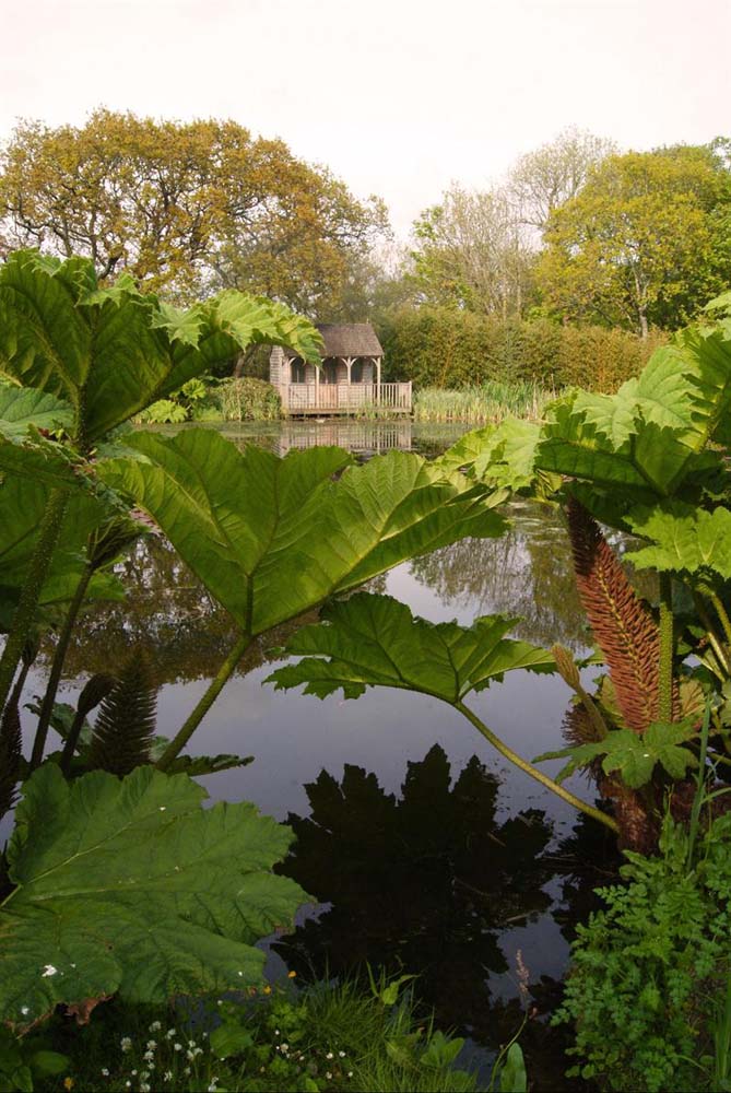 View of a summerhouse sat at the edge of the large pond through the canopy of leaves