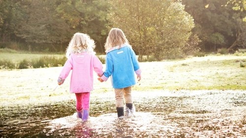 Two girls hand in hand walking through a large puddle