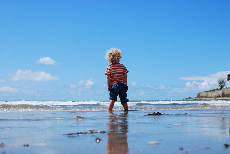 Male child with curly blonde hair standing by the sea