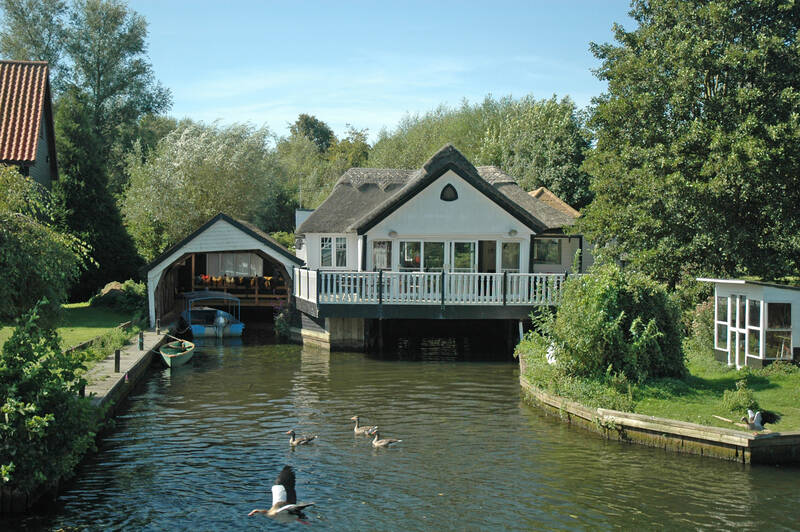 House sitting above the water with ducks in the foreground