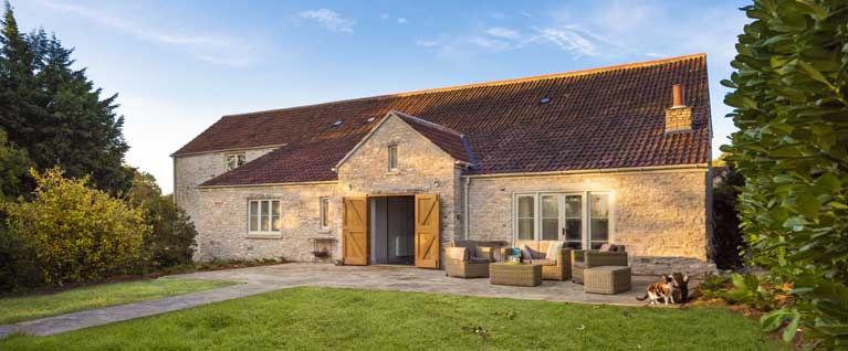 Frontage of a luxury holiday cottage with opened double doors and outdoor seating 